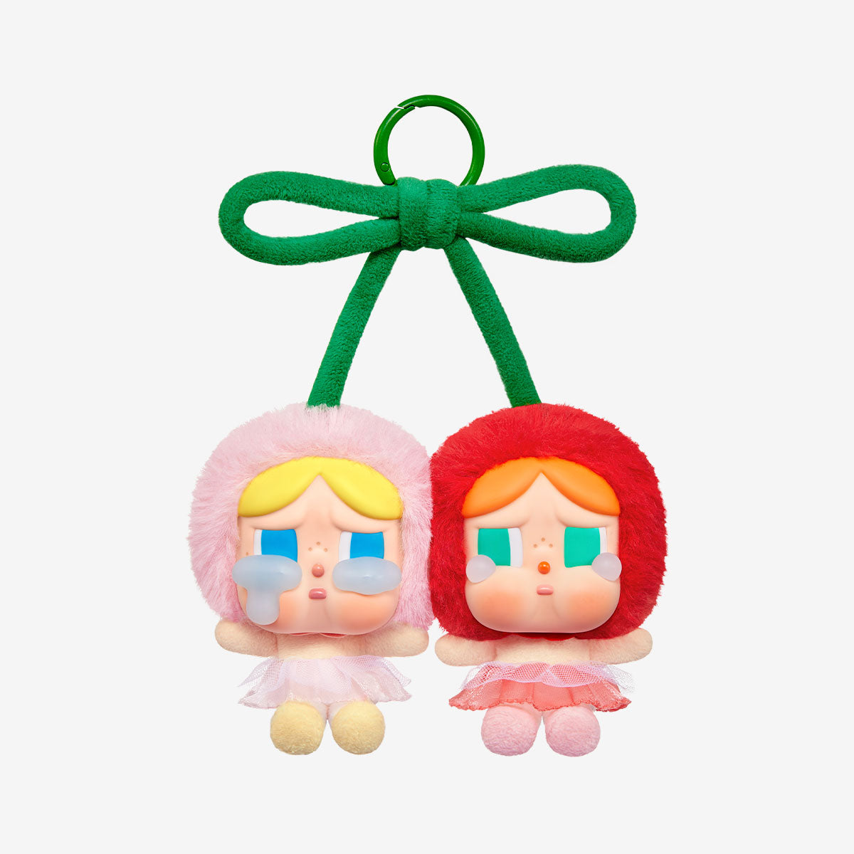 A cute double keychain featuring two plush figures with teary eyes, one in a pink outfit and the other in red, tied together with a green bow resembling cherries. Set against a plain white background.