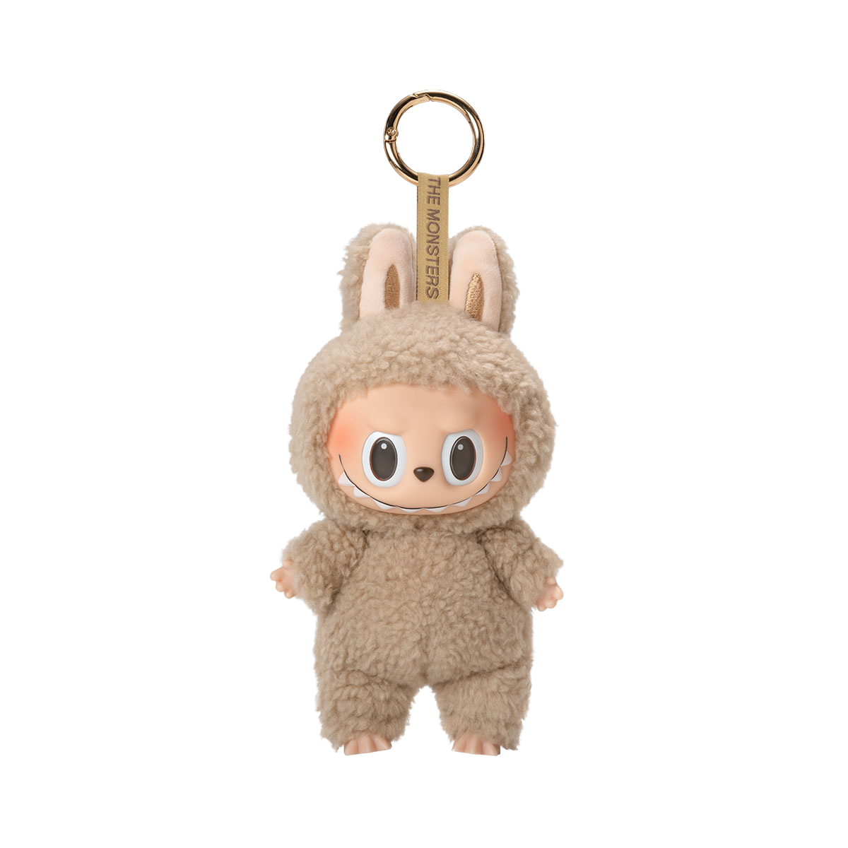 A fluffy light brown plush toy keychain of a character with a wide, mischievous smile, large black eyes, and bunny ears, with the text "THE MONSTERS" on the keyring strap.