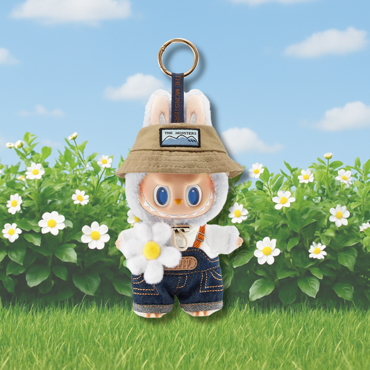 A charming collectible keychain figure from Pop Mart’s Labubu “The Monsters” series, posed in a cheerful garden setting. The character is dressed in a fuzzy white bunny suit with a beige bucket hat labeled “THE MONSTERS.” It wears denim overalls with stitched details and a white hoodie underneath, holding a soft plush daisy flower. The background features a sunny sky with fluffy clouds and a bush full of blooming white daisies, enhancing the character’s cute and outdoorsy aesthetic.
